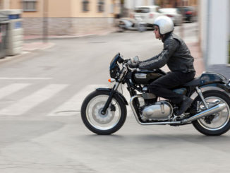 Ein Mann fährt auf einer schwarzen triumph_thruxtondurch die Straßen einer Stadt.