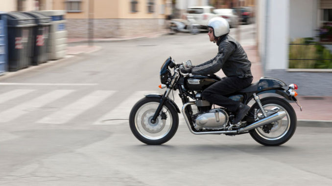 Ein Mann fährt auf einer schwarzen triumph_thruxtondurch die Straßen einer Stadt.