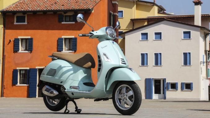 Eine türkise Vespa GTS 300 steht 2019 auf einem italienischen Dorfplatz.