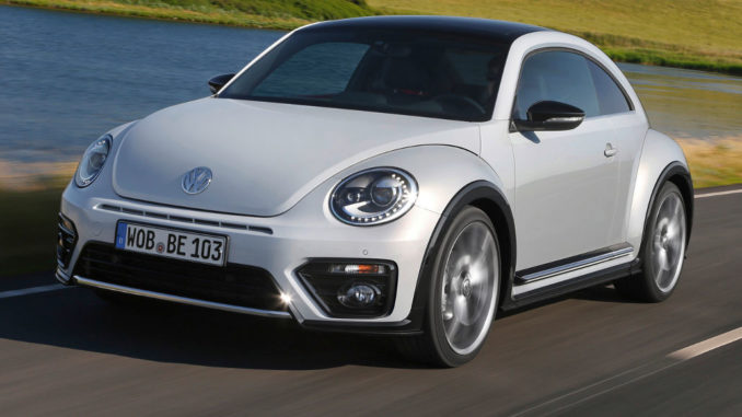 Ein weißer VW Beetle fährt 2016 ein Seeufer entlang.