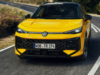 Ein gelber VW T-Roc der zweiten Generation fährt 2025 um eine Kurve auf einer Landstraße.