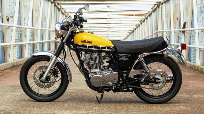 Eine gelbe Yamaha SR400 steht 2017 auf einer Brücke.